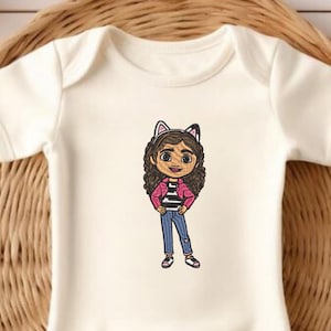 May include: White baby onesie featuring a cartoon illustration of a girl with brown hair wearing a pink jacket, black and white striped shirt, blue jeans, and cat ears.