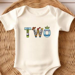May include: White baby onesie with the word "TWO" spelled out in colorful letters. Each letter is decorated with a different character from the Toy Story movie franchise.