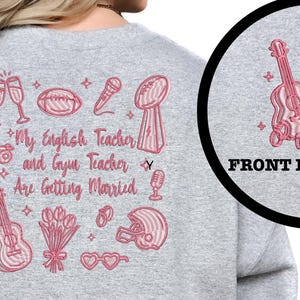 Puede incluir: Sudadera gris con diseño bordado en rosa. El diseño incluye copas de champán, un balón de fútbol americano, un micrófono, un trofeo, una guitarra, un ramo de flores, un casco de fútbol americano y el texto "My English Teacher and Gym Teacher Are Getting Married."