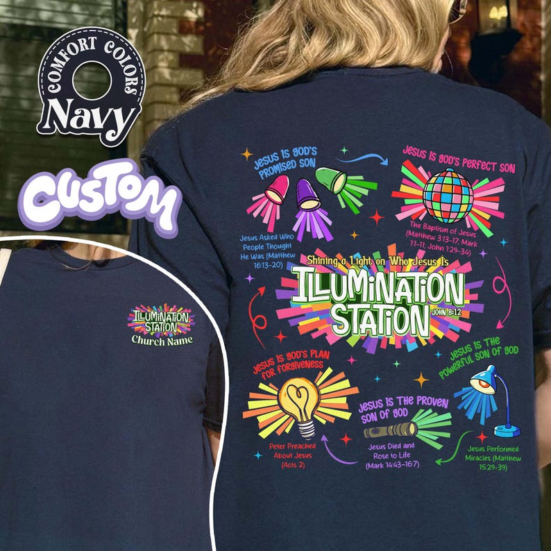 May include: Navy blue t-shirt with a colorful graphic design. The design includes the text "ILLUMINATION STATION" and various religious phrases and illustrations. The shirt also features the words "Comfort Colors" and "Custom".