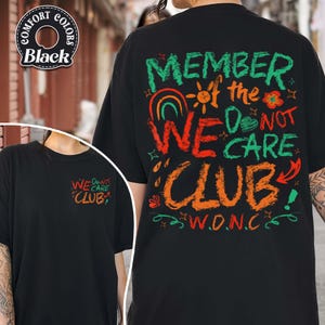 May include: Black t-shirt with the text "MEMBER of the WE DO NOT CARE CLUB" in colorful, handwritten-style lettering. The shirt also features the acronym "W.D.N.C." and a smaller version of the text on the front.