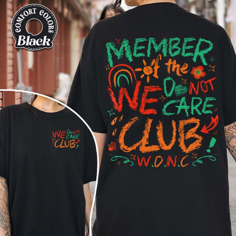 May include: Black t-shirt with the text "MEMBER of the WE DO NOT CARE CLUB" in colorful, handwritten-style lettering. The shirt also features the acronym "W.D.N.C." and a smaller version of the text on the front.