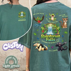 May include: Light green t-shirt with a Rainforest Falls graphic on the front and back. The back features a waterfall scene with various animals and the text "Exploring the Nature of God". The shirt also has the text "Amadora".