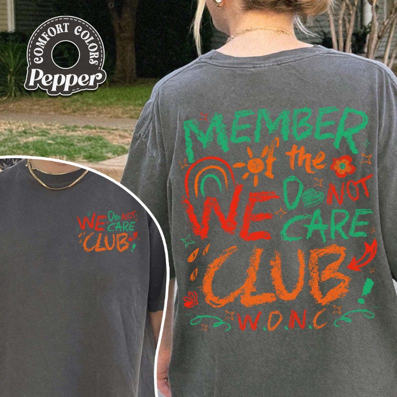 May include: A gray t-shirt with the text "MEMBER of the WE DO NOT CARE CLUB" in green, orange, and red. The shirt has a crew neck and short sleeves. The shirt also has the text "WE DO NOT CARE CLUB" on the front.