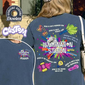 May include: A navy blue long-sleeve shirt with a colorful graphic design. The design includes the words "ILLUMINATION STATION" and various illustrations such as a disco ball, a lamp, and a flashlight. The shirt also has the text "Shining A Light On Who Jesus Really Is".