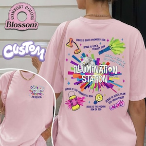 May include: A light pink t-shirt with the text "ILLUMINATION STATION" and various graphics. The back of the shirt features a colorful design with religious text and illustrations. The front of the shirt has a smaller version of the design with the name "JESSICA".