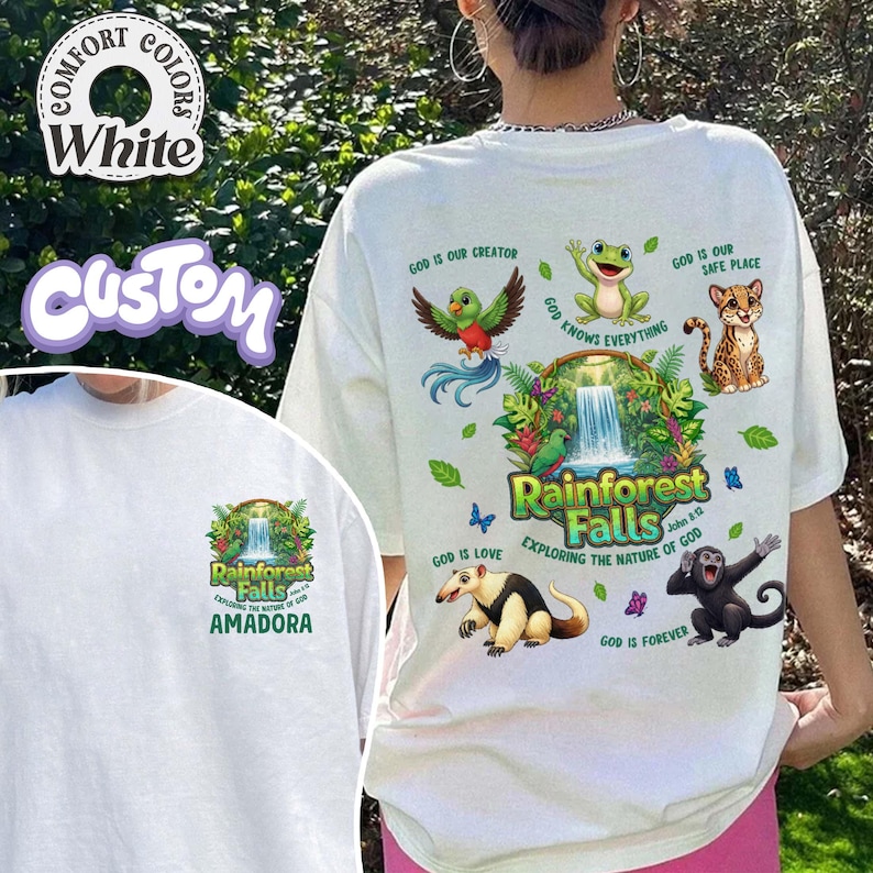 May include: White t-shirt featuring a vibrant rainforest-themed design. The graphic includes a waterfall, diverse animals, and the text "Rainforest Falls" and "Exploring the Nature of God". The shirt also has the text "AMADORA".