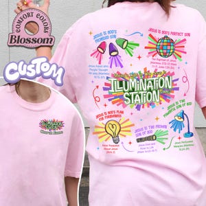 May include: A light pink t-shirt with a graphic design featuring the text "ILLUMINATION STATION" and various religious illustrations. The shirt also includes the text "Church Name" and other religious phrases.
