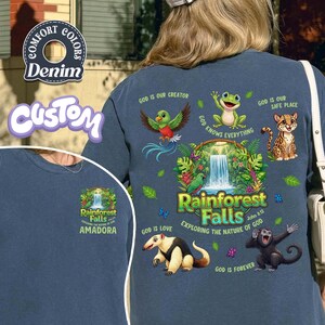 May include: Denim blue long-sleeve shirt with a colourful rainforest graphic. The design includes a waterfall, various animals, and the text "Rainforest Falls" and "Exploring the Nature of God". The shirt also features the text "Amadora".
