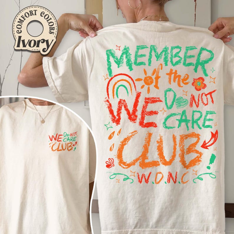 May include: Ivory-colored t-shirt with the text "MEMBER of the WE DO NOT CARE CLUB" in green, orange, and red. The design includes a rainbow, sun, and flower graphics. The front of the shirt has the text "WE DO NOT CARE CLUB".