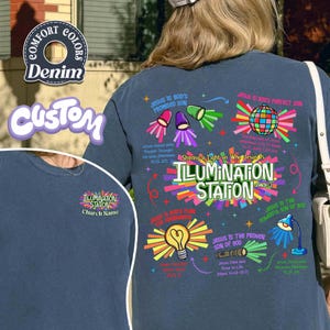May include: Denim blue t-shirt with colorful graphic designs and text. The back of the shirt features the words "ILLUMINATION STATION" and religious themed illustrations. The front of the shirt has the words "ILLUMINATION STATION" and "Church Name".