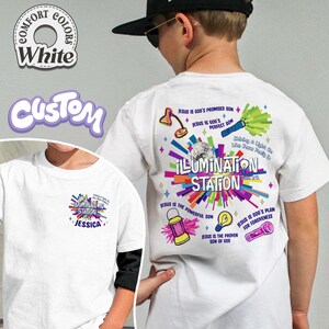 May include: White t-shirt with a colorful graphic design on the back that says "ILLUMINATION STATION" with various religious symbols and text. The front of the shirt has a smaller version of the design with the name "JESSICA".