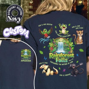 May include: Navy blue t-shirt with a vibrant rainforest design, including the text "Rainforest Falls" and animal illustrations. The shirt also features the text "Exploring the Nature of God" and other religious phrases.