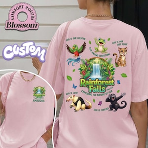 May include: Pale pink t-shirt with a vibrant rainforest design on the back, including a waterfall, various animals, and the words "Rainforest Falls". The front has a smaller version of the graphic. The shirt also has the text "God is our creator".