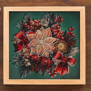 May include: A framed, beaded Christmas ornament with a central flower design in shades of tan and gold. The ornament features red bows, berries, and decorative elements on a green background, all within a light wood frame.