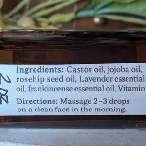 Puede incluir: Una botella de vidrio marr&oacute;n con una etiqueta blanca que muestra los ingredientes y las instrucciones de uso. La etiqueta enumera aceite de ricino, aceite de jojoba, aceite de semilla de rosa mosqueta, aceite esencial de lavanda, aceite esencial de incienso y vitamina E. La botella es de 59 ml.