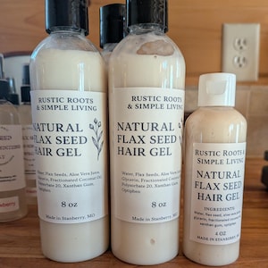 Puede incluir: Botellas de gel capilar Natural Flax Seed de Rustic Roots & Simple Living. Las etiquetas enumeran los ingredientes y el tamaño de las botellas, que son 237 ml y 118 ml. El gel es de color crema.