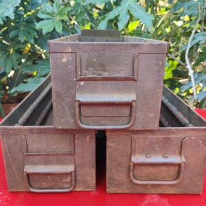 May include: Three stacked metal storage boxes with rusty brown paint and metal handles. The boxes are empty and have a worn, vintage look.