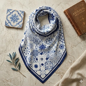 May include: A white and blue patterned silk scarf with a dark blue border. The scarf features a repeating design of floral and geometric patterns. A decorative tile and a book titled "AZULEJOS: ART & HISTORY" are also in the image.