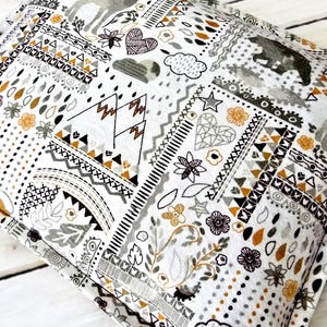 May include: A white fabric pillow with a gray and gold geometric pattern. The pattern includes mountains, stars, hearts, and other abstract shapes.
