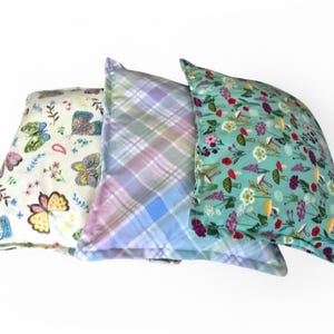 May include: Three decorative throw pillows with different patterns. One pillow has a butterfly design, another has a plaid pattern, and the third features a floral and mushroom print. The pillows are in shades of blue, green, pink, and yellow.
