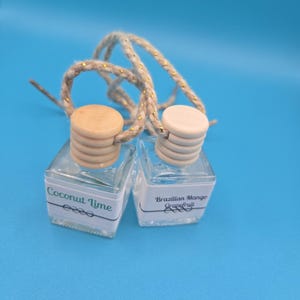 Puede incluir: Dos peque&ntilde;os frascos de vidrio transparente con tapas de madera y cuerdas para colgar. Una etiqueta dice "Coconut Lime", la otra "Brazilian Mango Grapefruit". Los frascos est&aacute;n sobre un fondo azul.