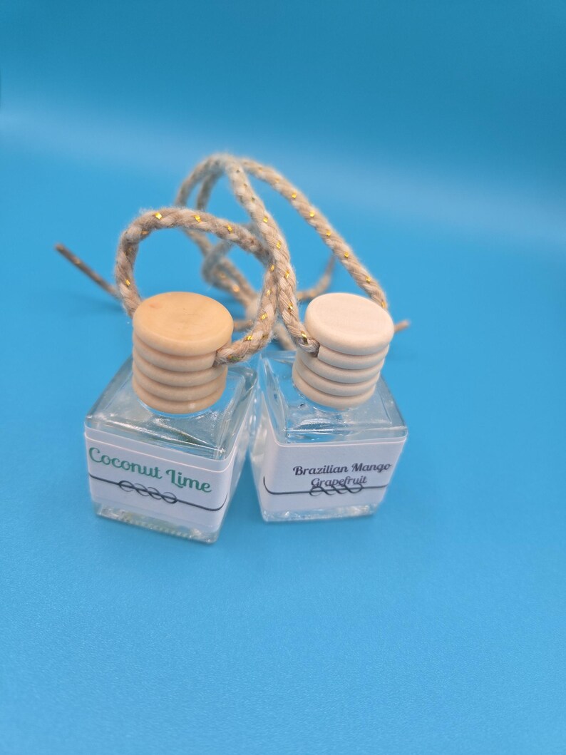 Puede incluir: Dos peque&ntilde;os frascos de vidrio transparente con tapas de madera y cuerdas para colgar. Una etiqueta dice "Coconut Lime", la otra "Brazilian Mango Grapefruit". Los frascos est&aacute;n sobre un fondo azul.