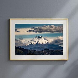 Puede incluir: Una fotograf&iacute;a enmarcada de un pico de monta&ntilde;a cubierto de nieve con nubes en el cielo. La monta&ntilde;a est&aacute; rodeada de colinas verdes y un peque&ntilde;o pueblo.
