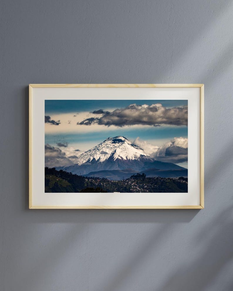 Puede incluir: Una fotograf&iacute;a enmarcada de un pico de monta&ntilde;a cubierto de nieve con nubes en el cielo. La monta&ntilde;a est&aacute; rodeada de colinas verdes y un peque&ntilde;o pueblo.