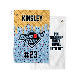 May include: A white and blue pin trading/rally towel with a waffle pattern and a baseball-themed logo that says "Diamond Elite" with a red baseball and the number "23". The towel is 11 inches by 18 inches.