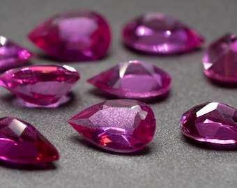 May include: A collection of pink gemstones, some are pear-shaped and others are round, all are faceted and have a high shine.