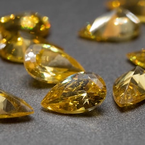 May include: A group of yellow pear-shaped gemstones on a gray surface. The gemstones are faceted and have a high shine.