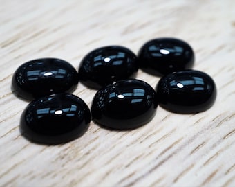 Könnte beinhalten: Sechs schwarze ovale Cabochon-Edelsteine auf einer hellen Holzoberfläche.