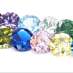May include: An array of colorful gemstones in various shades, including pink, purple, blue, green, and yellow. The round-cut gems are arranged closely together, showcasing their facets and brilliance against a white background.