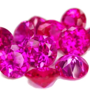 Puede incluir: Un grupo de piedras preciosas redondas y facetadas de color rosa. Las piedras preciosas están dispuestas en un racimo, con algunas superpuestas.