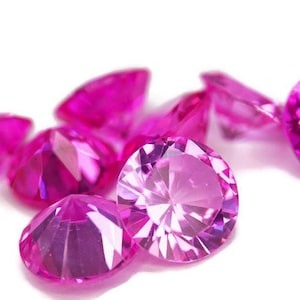 Puede incluir: Un grupo de piedras preciosas rosas, talladas en forma redonda, con facetas que reflejan la luz.