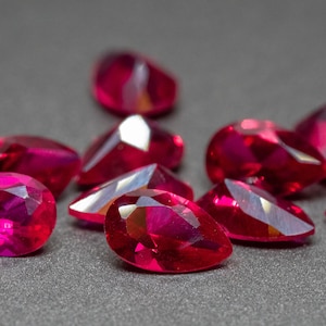 Op de afbeelding: Een groep peer-vormige, gefacetteerde robijn edelstenen in verschillende maten, getoond op een grijs oppervlak.