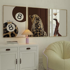 May include: Three framed wall art pieces. The first features a brown and white 8-ball design with the text "lucky you". The second depicts a leopard. The third shows a cocktail glass. All are in gold frames.