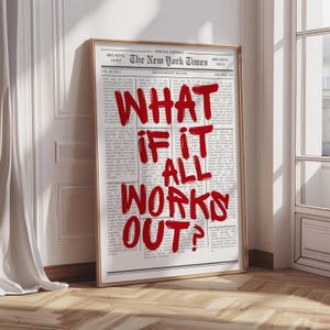 以下が含まれることがあります： 「The New York Times」の新聞記事を額装したプリント。赤いテキストで「WHAT IF IT ALL WORKS OUT？」と書かれています。プリントは金色のフレームに入っており、白い壁に立てかけられています。