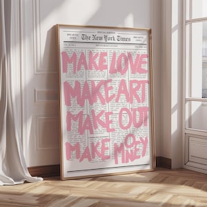 Puede incluir: Una impresión enmarcada de una página del periódico New York Times. Texto rosa intenso superpuesto en el periódico, con las palabras "MAKE LOVE, MAKE ART, MAKE OUT, MAKE MONEY". La impresión está en un marco dorado.