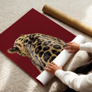 May include: A large, burgundy-colored art print featuring a detailed leopard pattern. The print is partially unrolled, revealing a glimpse of the animal's spotted fur. A rolled-up poster and a white roll of paper are also visible.