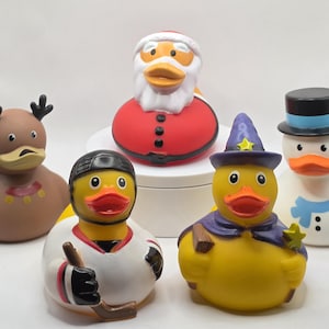 May include: A collection of rubber duck toys, each uniquely designed. One duck is dressed as Santa Claus, another as a snowman, and a third as a hockey player. Other ducks are styled as a reindeer and a wizard.