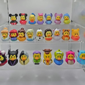 May include: A collection of colorful rubber duck toys, each designed to resemble popular cartoon characters. The ducks are arranged on a clear, multi-tiered display shelf. The characters include Mickey and Minnie Mouse, and other Disney characters.