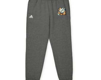 Può includere: Pantaloni della tuta Adidas grigio antracite con logo Adidas bianco sulla gamba sinistra. Una piccola toppa sulla tasca destra presenta un disegno di biscotti con la scritta "misf". I pantaloni della tuta hanno una vita con coulisse e polsini.