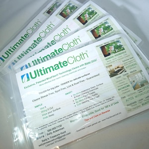 May include: A close-up of a package of Ultimate Cloth microfiber cleaning cloths. The package is white with green text and a green leaf logo. The text on the package reads "Exclusive, Patented MiraFiber Technology Cleans with Water Only!" and "TOUGH for big jobs - TENDER for delicate surfaces". The package also includes a list of surfaces that the cloths can be used to clean, such as windows, mirrors, glass, and stainless steel.