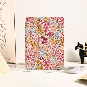Pode incluir: Uma capa para tablet com padrão floral, com fundo branco e flores rosa, laranja e azuis.