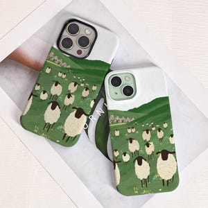 Puede incluir: Dos fundas de teléfono con un diseño caprichoso que presenta un rebaño de ovejas pastando en una ladera verde bajo un cielo blanco. Las fundas tienen una sección superior blanca y una sección inferior verde con la ilustración de las ovejas.