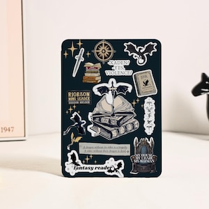 Puede incluir: Una hoja de pegatinas de color verde oscuro con ilustraciones de fantasía. Los diseños incluyen dragones, libros, una brújula, una espada y texto que dice "Fantasy Reader" y "My House, My Chair, My Woman."