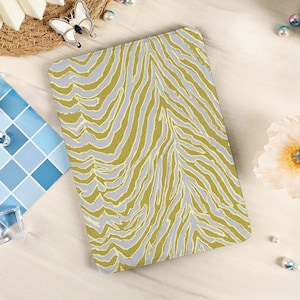May include: A rectangular, patterned item with a zebra stripe design in shades of olive green and gray. The item is set against a light-colored background, with decorative elements like a butterfly brooch, pearls, and a flower. The overall aesthetic is modern and stylish.