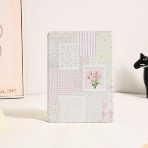 以下が含まれることがあります： ピンクと白のパッチワークのデザインで、花柄のモチーフが施されています。デザインには、ギンガムチェック、ストライプ、花柄など、さまざまなパターンが使用されています。デザインの中央には、ピンクのチューリップのブーケが描かれています。